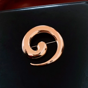 Macro shot of gold spiral brooch with polished finish on black leather texture background