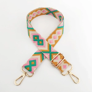 Detail of embroidered geometric bag strap with golden metal hooks on white background