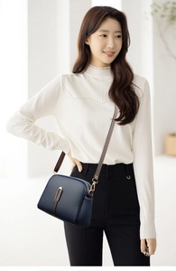 Detail of dark blue shell-shaped shoulder bag with brown strap and gold metal hardware