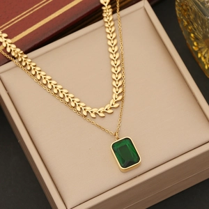 Macro detail of a double-layered gold necklace featuring a green emerald pendant on a jewelry box