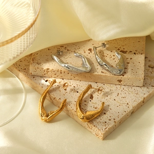 Detail of irregular lava texture earrings in gold and silver on a beige stone slab