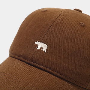 Detailed close-up of premium brown cotton baseball cap with white polar bear embroidery