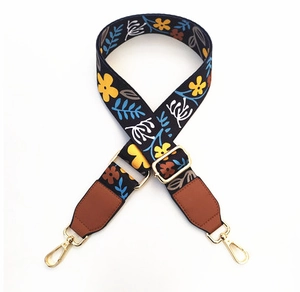 Detailed texture of black floral bag strap with gold metal buckles and brown leather ends