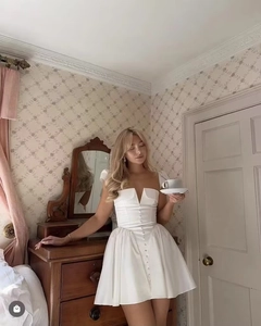 Close-up of elegant white mini dress with pearl buttons and structured satin bodice