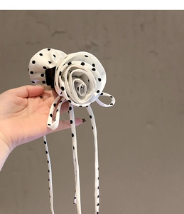 Detailed view of hand holding a white polka dot fabric rose hair claw clip with long tassels