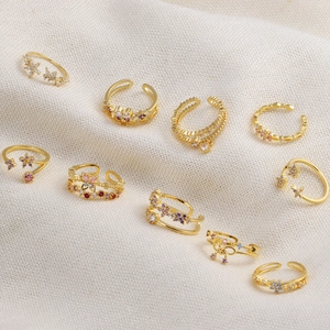Vue à plat de bagues dorées papillon et fleur avec zircons colorés sur fond blanc