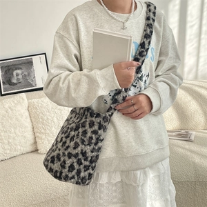 Detail of plush leopard print shoulder bag worn by model in a cozy indoor setting