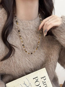 Détail d'un collier de perles vintage marron et ambre sur un pull en maille beige