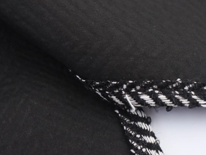 Close-up of black textured fabric with white stitching and fringe detail on the coat