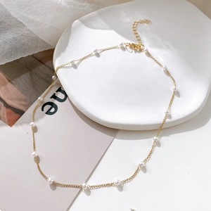 Detail of elegant gold chain necklace with evenly spaced white pearls and lobster clasp