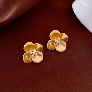 Macro shot of gold-plated matte flower earrings with sparkling zircon center details