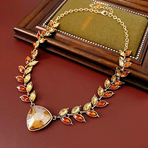 Détail de collier vintage doré avec pampilles en cristal ambré sur cuir rouge foncé