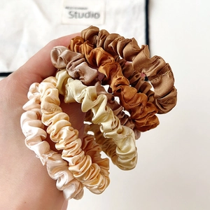 Set of four gradient silk satin hair scrunchies held by hand showing smooth texture
