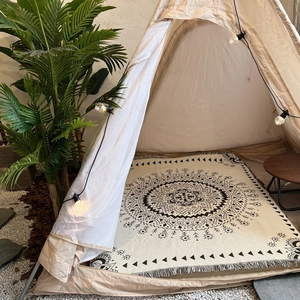 Detail view of a bohemian woven blanket with mandala patterns and tassels inside a cozy tent