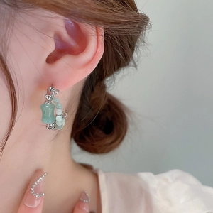 Close-up of silver hoop earring with green beads and gourd pendant on model's ear
