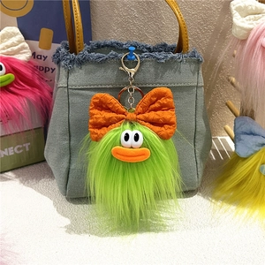 Dettaglio di un mostro di peluche verde con fiocco arancione su borsa di jeans