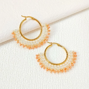 Detail of handmade fan-shaped gold earrings with white pearls and peach faceted beads