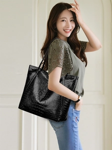 Detail of a black crocodile pattern tote bag shown on a female model for daily commute