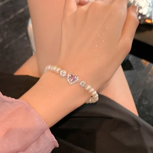 Détail du bracelet élastique en perles avec zircon cœur rose porté au poignet féminin