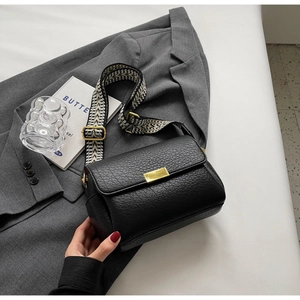 Détail du sac bandoulière en cuir noir avec large sangle tissée géométrique