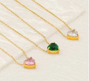 Detailed view of three heart-shaped gemstone necklaces in white, green, and pink gold plating