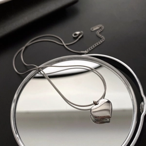 Macro detail of silver heart pendant and sleek snake chain on a reflective mirror