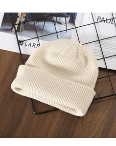 Close-up of beige ribbed knit beanie texture on a minimalist wooden background