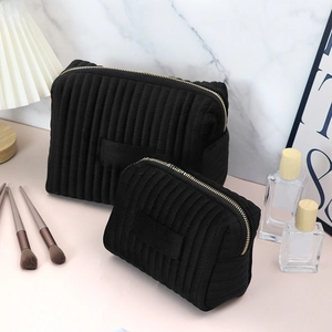 Detail of two black quilted velvet cosmetic bags in different sizes with gold zippers