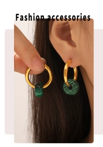 Close-up of 18k gold earrings with cylindrical malachite stones worn on a model ear