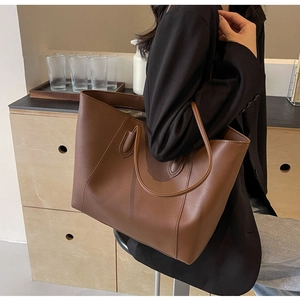 Brown leather tote bag held by a model in a black blazer, showing its large capacity