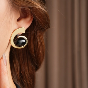 Gros plan d'une boucle d'oreille géométrique dorée avec pierre noire sur un modèle
