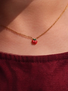 Dettaglio di una collana dorata con un simpatico ciondolo a mela rossa su una modella