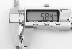 Digital caliper measuring the 5.84 mm thickness of the wavy stainless steel cross pendant