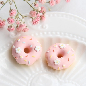 Makroaufnahme von zwei rosa Donut-Anhängern aus Harz mit Blumendetails in weißer Schale