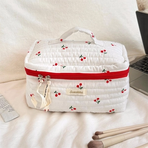 Detail of white quilted toiletry bag with cherry print and red zipper handle
