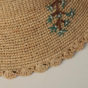 Detail of hand-woven raffia hat with floral embroidery and white pearl accents