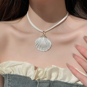 Close-up of a white shell pendant with gold clasp on a minimalist white leather cord