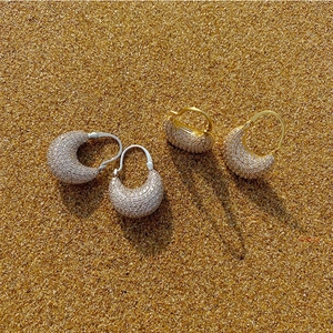 Macro shot of gold and silver pave zircon crescent hoop earrings on golden sand
