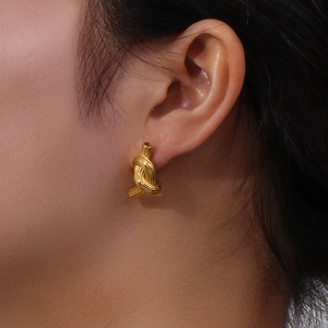 Detailed view of model wearing golden knotted button earrings in brushed stainless steel