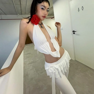 Dettaglio del top bianco con balze e gonna a pieghe con elegante accessorio floreale