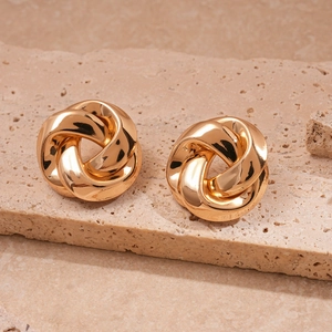 Macro detail of golden geometric knot earrings on a textured stone display surface