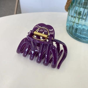 Detail of a large purple pumpkin hair claw with a durable golden spring on a white desk