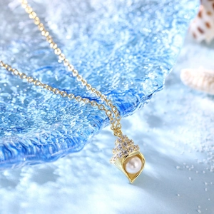 Detailed view of conch shell pendant with pearl and zircon on a blue glass plate