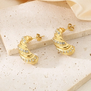 Macro view of C-shaped golden twisted earrings with crystals on stone and silk background