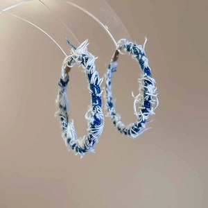 Macro shot of large blue denim C-shaped hoop earrings with stylish frayed edge texture