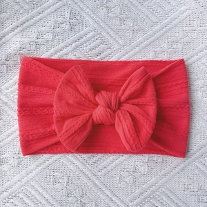 Detail of red cable knit baby headband with oversized bow on white lace background