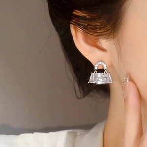 Close-up of silver handbag-shaped earring with sparkling rectangle crystals on a model