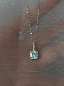Macro shot of a silver necklace featuring a square blue stone pendant with halo setting