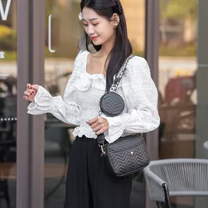 Close-up of black V-quilted crossbody bag with a round coin pouch and wide jacquard strap