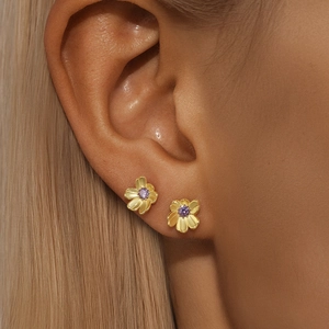 Detail of gold flower earrings with purple zircons worn on the lobe and cartilage